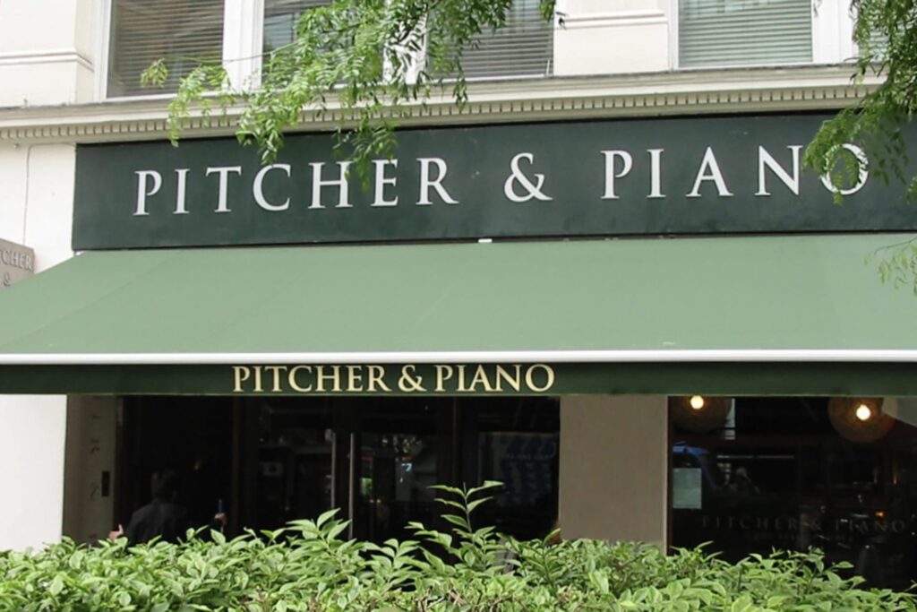 sage green commercial awning installed beneath a branded sign that reads "pitcher & piano"