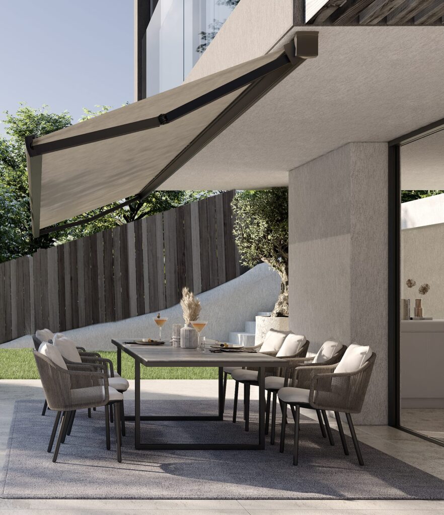 Table and chairs set for an al fresco lunch, shaded by an Epica Lite awning with a textured light grey fabric