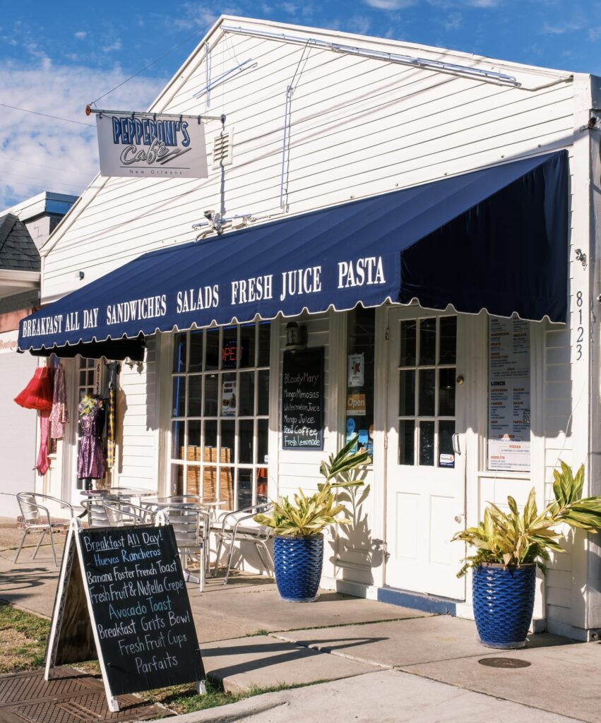 A white building with a large dark blue commercial canopy installed over the windows and doors. The commercial canopy has printed text on it describing the kind of food that business sells.